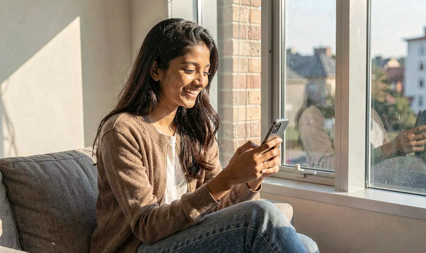 Young Bangladeshi woman smiling while using the 71OK casino app on her smartphone in a bright modern indoor setting